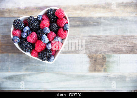 Gesunder frischer Obstsalat mit Erdbeeren, Brombeeren, Heidelbeeren und Himbeeren. in Herz-Form-Schüssel. Stockfoto