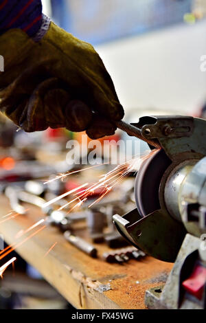 Mechaniker Polieren eine Schraube am industriellen Poliermaschine in einer Garage. Sparks entstammen Schleifscheibe. Stockfoto