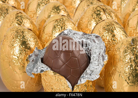 über Nachsicht in Schokolade Ostereier eingewickelt in glänzender Goldfolie in Reihen bereit für Schokoholiker Übergewicht Gesundheitsproblem Stockfoto