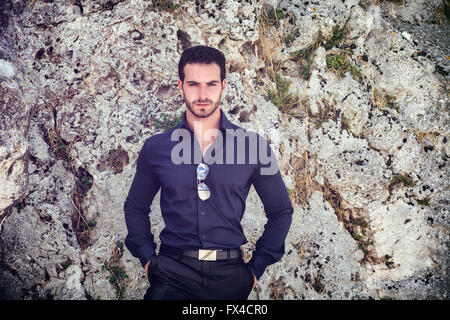 Eine halbe Stelle erschossen eines wunderschönen jungen Geschäftsmann gegen Boulder mit Händen in den Taschen und in die Kamera schaut. Stockfoto