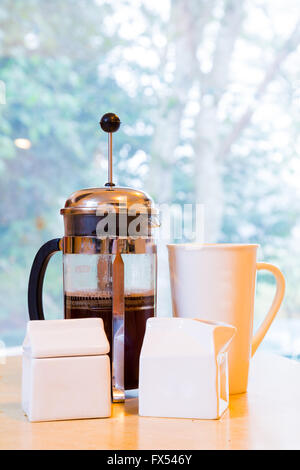 Kaffee wird in den frühen Morgenstunden in einem französischen Presse zusammen mit Sahne und Zucker auf dem Küchentisch gemacht. Stockfoto