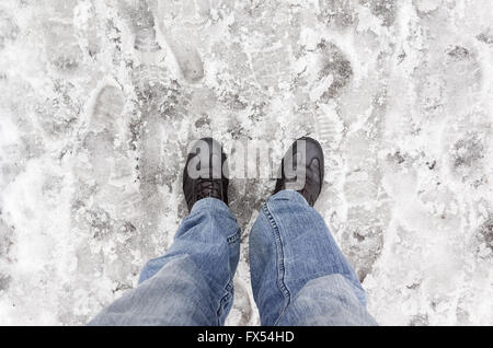 Männliche Füße in Blue Jeans auf nassen schmutzigen Schnee stehen Stockfoto