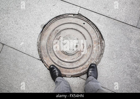 Füßen ein Städter Mannes in schwarz glänzender neue Schuhe auf rostigen Kanalisation Schacht Stockfoto