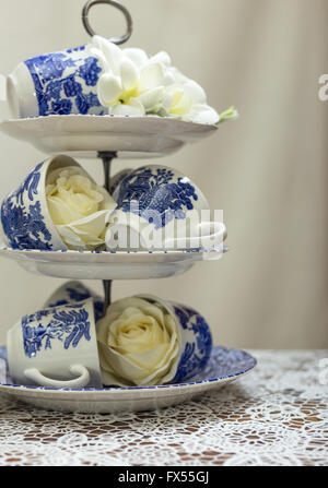 Blaue und weiße Weide-Muster-Etagere und Tassen auf Lace-Tuch für Hochzeit Nachmittagstee mit Rosen und bouquet Stockfoto