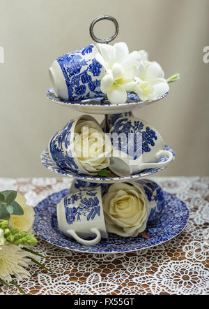 Blaue und weiße Weide-Muster-Etagere und Tassen auf Lace-Tuch für Hochzeit Nachmittagstee mit Rosen und bouquet Stockfoto