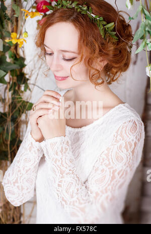 Junge rothaarige Braut im Grünen Kranz sanft lächelnd, faltete die Hände im Gebet. Stockfoto