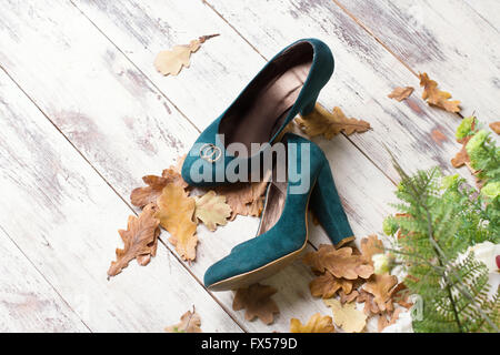 Trauringe auf grünem Veloursleder Schuhe. Hölzerne Hintergrund mit Herbstlaub und grünem Farn. Stockfoto