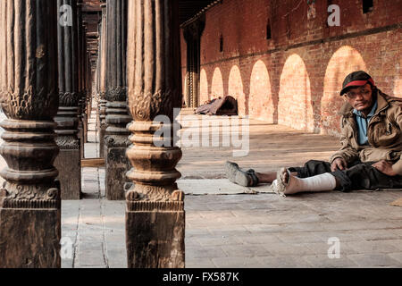 Ein armer Mann mit einem gebrochenen Bein ruht in einem öffentlichen Gebäude in Kathmandu Stockfoto