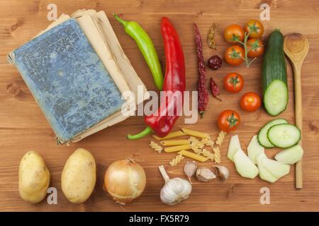 Am alten Kochbuch Rezepte auf einem Holztisch. Gesundes Gemüse zu kochen. Zubereitung von Speisen nach Hause Diät. Verschiedene Arten von Gemüse. Stockfoto