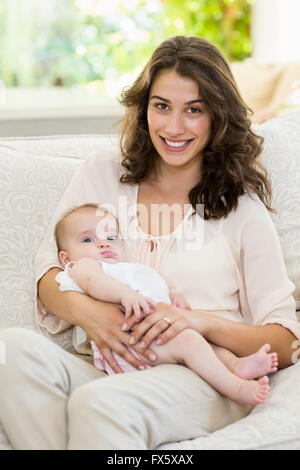 Mutter hält ihr Baby auf Schoß im Wohnzimmer Stockfoto