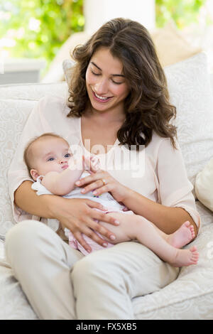 Mutter hält ihr Baby auf Schoß im Wohnzimmer Stockfoto