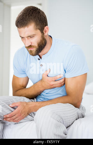 Junger Mann mit Schmerzen in der Brust im Bett Stockfoto