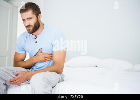 Junger Mann mit Schmerzen in der Brust auf Bett Stockfoto