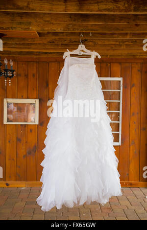 Weißes Brautkleid von einem Träger in einer Scheune hängen. Stockfoto