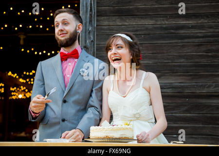 Braut und Bräutigam schneiden Sie den Kuchen und füttern einander am Tag ihrer Hochzeit an der Rezeption. Stockfoto