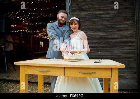 Braut und Bräutigam schneiden Sie den Kuchen und füttern einander am Tag ihrer Hochzeit an der Rezeption. Stockfoto