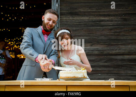 Braut und Bräutigam schneiden Sie den Kuchen und füttern einander am Tag ihrer Hochzeit an der Rezeption. Stockfoto