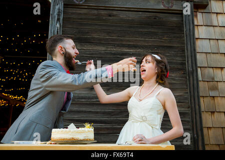 Braut und Bräutigam schneiden Sie den Kuchen und füttern einander am Tag ihrer Hochzeit an der Rezeption. Stockfoto