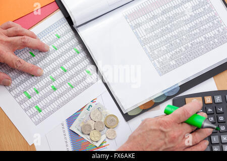 Beschäftigt Finanzier an seinem Schreibtisch mit einen Taschenrechner, einen Umsatzbericht mit Bargeld lose Verlegung oberste Sicherheitsebene eines Diagramms zu überprüfen Stockfoto