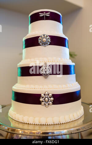 Große weiße Hochzeitstorte eingewickelt in lila Band mit Broschen an jeder Stufe des Desserts befestigt. Stockfoto