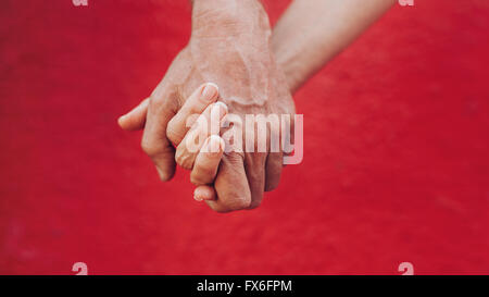Nahaufnahme von Mann und Frau, die Hand in Hand vor rotem Hintergrund. Liebevolle paar Hand in Hand. Stockfoto