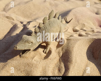 Spielzeug in Form von einem Dinosaurier stehend auf Sand. Stockfoto