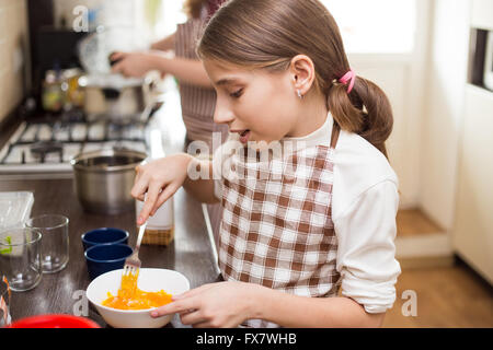 Kleinen Mädchens in Schürze schlagen von Eiern in weiße Schüssel in der Küche Stockfoto