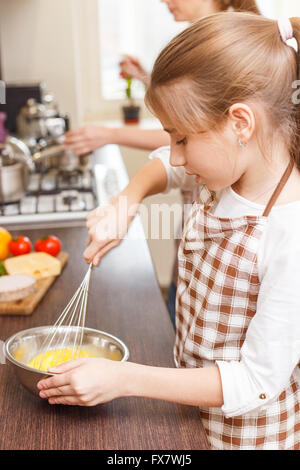 Kleines junges Mädchen entführt Eiern in die Schüssel in der Küche. Mutter und Tochter Kochen Frühstück zusammen Stockfoto