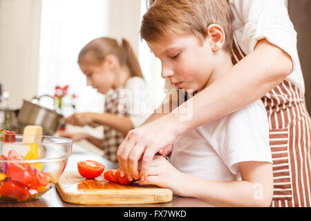 Kleiner Junge schneiden in Scheiben Gemüse für Salat mit seiner Mutter in der Küche Familie kochen Hintergrund Stockfoto