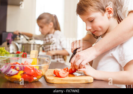 Kleiner Junge schneiden in Scheiben Gemüse für Salat mit seiner Mutter in der Küche Familie kochen Hintergrund Stockfoto