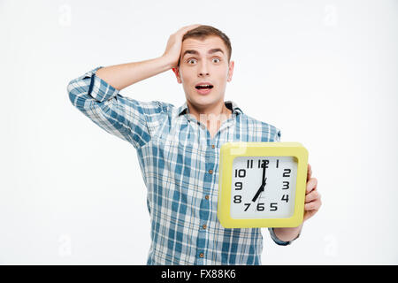 Schockiert begeistert junge Mann hält die große Uhr über weißem Hintergrund Stockfoto