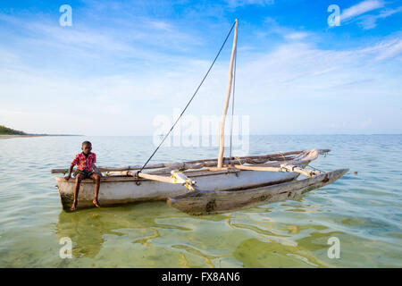 Ein kleiner Junge sitzt auf dem Heck einer kleinen Dhau auf der Küste von Sansibar Ostafrika Stockfoto