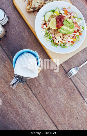 Frischer Salat auf einem Holztisch mit Besteck und Servietten Stockfoto