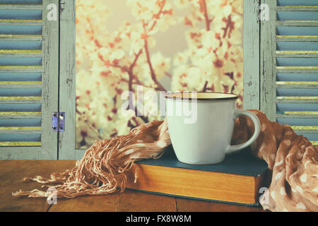 romantische Szene Tasse Kaffee neben alten Buch vor Blick auf die Landschaft außerhalb des alten rustikalen Fensters. Jahrgang gefiltert Stockfoto