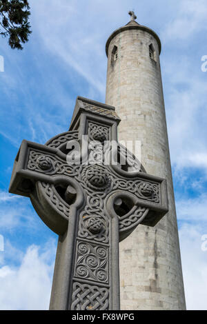 Ein Stein steht Keltisches Kreuz über einem Grab auf dem Glasnevin Cemetery in Dublin mit Daniel O'Connell Turm im Hintergrund Stockfoto