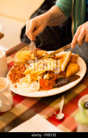 Ein junger Mann, ein komplettes englisches Frühstück - Eiern, Würstchen, Bohnen, Blutwurst, Chips, Tomaten, Toast, - in der Express Cafe Essen, besaß ein kleinen selbstständig Fisch und Pommesbude. Aberystwyth Wales UK Stockfoto