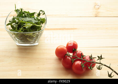 Cherrys Tomaten neben einer Glasschale mit grünen Blättern Stockfoto