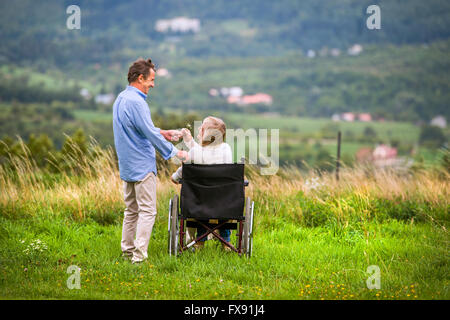 Ältere Mann mit Frau im Rollstuhl, grün Herbst Natur Stockfoto