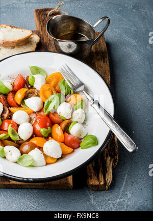 Italienische Caprese-Salat mit Cherry-Tomaten, kleine Mozzarella und frischem Basilikum in weißer Emaille Teller auf rustikalem Holzbrett über g Stockfoto