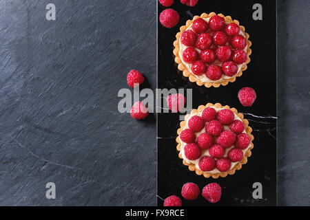 Zwei Törtchen mit Vanillesoße und frischen Reifen Himbeeren, serviert auf schwarzem Marmor Stein Schieferoberfläche. Mit textfreiraum an Stockfoto