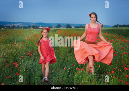 zwei Mädchen im roten Kleid zu Fuß auf Mohnfeld Stockfoto