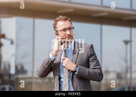 Geschäftsmann zu Fuß neben dem Unternehmen bauen und am Smartphone sprechen Stockfoto