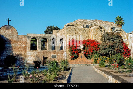 Leuchtende Bougainvillea Blumen umgeben eine Statue des spanischen Missionar Junipero Serra umarmt einen jungen, ein 1914 Denkmal des amerikanischen Künstlers Tole Van Rensaalar im Hof der Mission San Juan Capistrano in Orange County, Kalifornien, USA. Der sagenumwobene Franziskanermönch gründete die Mission im Jahr 1776, der siebte von 21 California Missionen nach oben und unten den Staat gegründet, um Spaniens Gebiet zu erweitern und die Indianer zum Christentum zu bekehren. Pater Serra wurde heilig gesprochen, als ein katholischer Heiliger von Papst Francis in 2015. Stockfoto