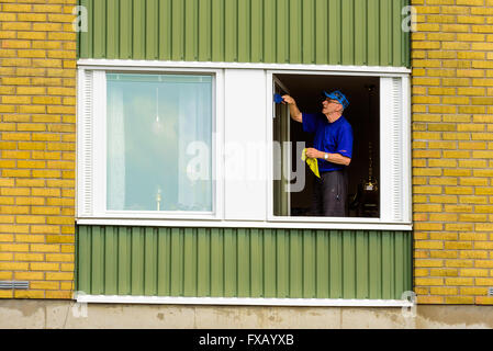 Lyckeby, Schweden - 7. April 2016: Senior woman Fensterputzen in einer Wohnung. Das Fenster ist geöffnet und der Mann ist von Wasser her Rechen Stockfoto
