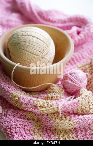Gestreifte schöne Schal und zwei Kugeln des Garns auf einem weißen Tisch. Kugeln aus Garn in einer Holzschale liegen. Garn ist rosa und IG Stockfoto