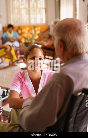 Alte Menschen in geriatrischen Hospiz: junge attraktive hispanic Frau arbeitet als Krankenschwester kümmert sich ein senior Mann im Rollstuhl. Sie Stockfoto