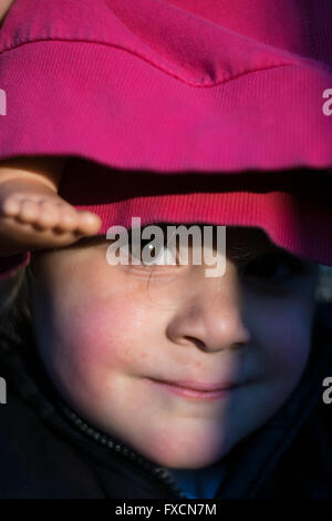 Porträt eines Mädchens versteckt unter einer Puppe in rot gekleidet. Stockfoto