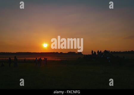 Menschen beobachten den Sonnenaufgang neben Stonehenge am Morgen der Sommersonnenwende. Stockfoto