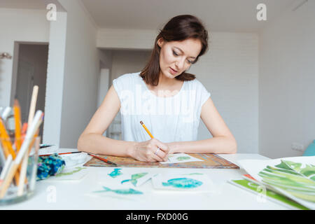 Hübsche Frau Maler sitzen und Skizzen mit Bleistift am Tisch im Kunstatelier konzentriert Stockfoto