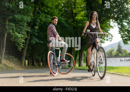 Register, um seinen Kopf zu drehen nach einer schönen jungen Frau, die mit dem Fahrrad in einer Gasse mit grünen Bäumen geht Stockfoto